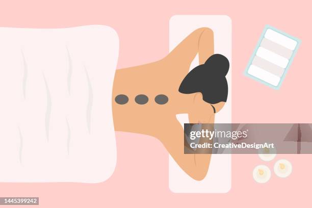 draufsicht der jungen frau mit hot stone massage auf dem spa-bett. entspannungs- und spa-konzept - massage stock-grafiken, -clipart, -cartoons und -symbole