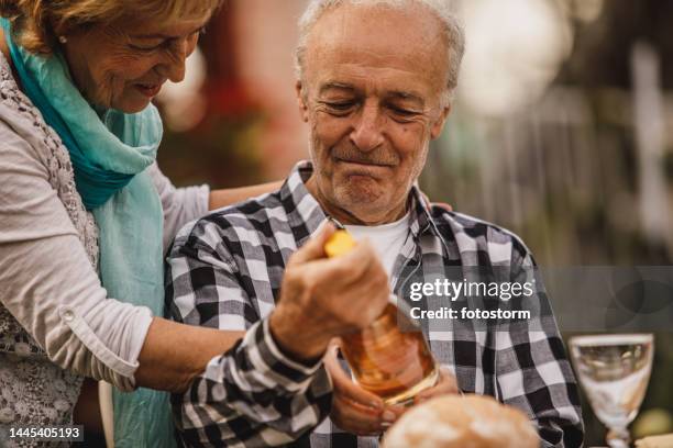 romantic senior couple having bonding moments before opening a bottle of white wine to enjoy with dinner - receiving present stock pictures, royalty-free photos & images