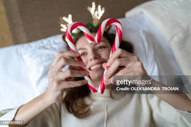 young woman with red christmas candy sticks in hear shape, laying on the bed - serre tête photos et images de collection