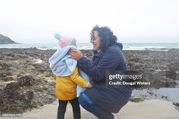a mother with her daughter at the beach on a stormy day - mother protecting from rain stock pictures, royalty-free photos & images