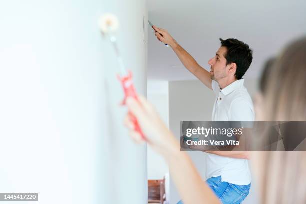 side view of pregnant couple refurbishing white background wall at home. - white paint roller stock pictures, royalty-free photos & images