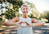 Fitness, happy and heart hands of old woman in nature after running for health, wellness and workout. Smile, motivation and peace with senior lady and sign for love, faith and training in nature