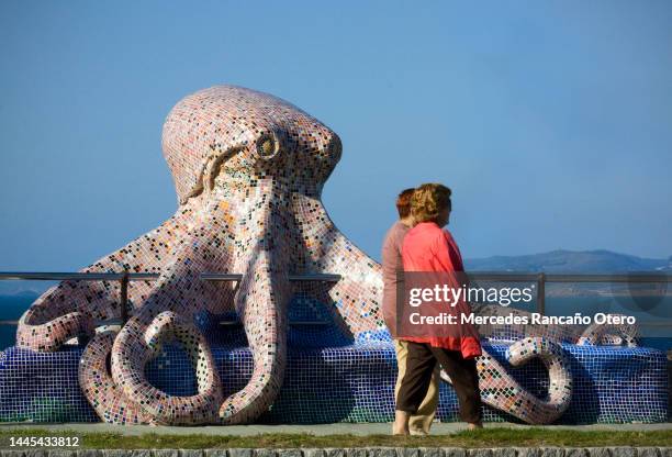 rear view of two middle aged women walking together passing by octopus  sculpture in a sea waterfront promenade.  a coruña city, galicia, spain. - la coruña imagens e fotografias de stock