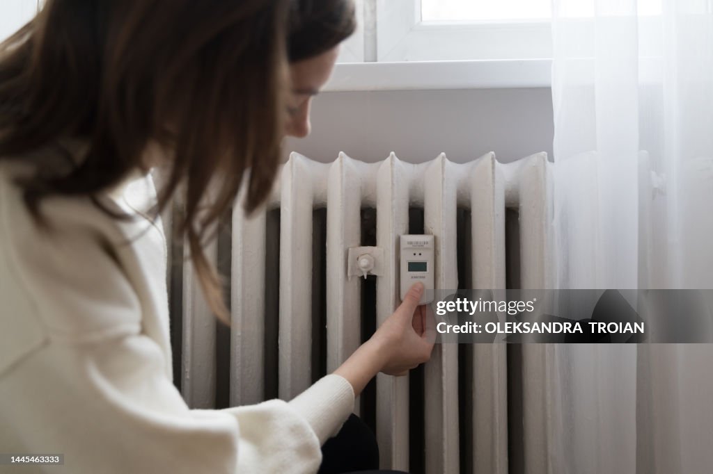 Young woman near the home radiator with temperature sensor