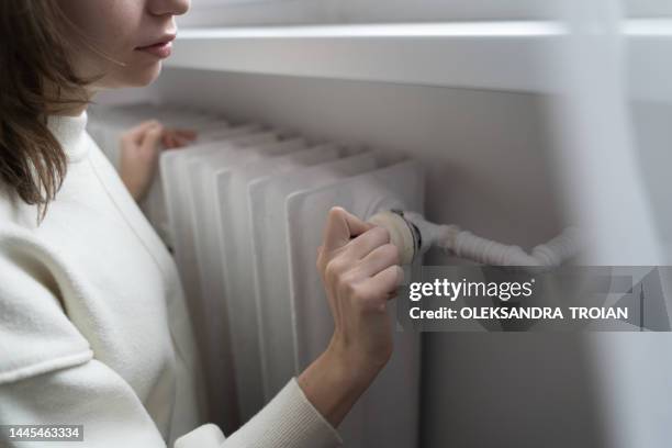 young woman near the home radiator with temperature termostat - lowering stockfoto's en -beelden