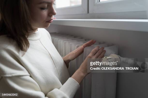 young woman near the home radiator with temperature termostat - lowering photos et images de collection