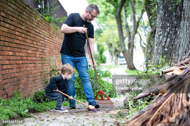 toddler son helping his father to sweep the sidewalk in front of the house - sweeping sidewalk stock pictures, royalty-free photos & images