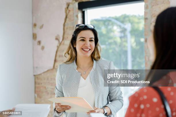 mid adult female real estate agent smiles at unrecognizable female client - contrato de arrendamento imagens e fotografias de stock