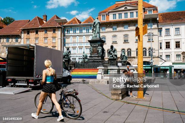 young woman walking with her bicycle and other people sitting by the archduke johann fountain (erzherzog-johann-brunnen) in the main square (hauptplatz) during the csd graz parade and parkfest. - estiria austria stock-fotos und bilder