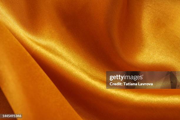 gold satin textured background with waves and folds. yellow cloth material backdrop for luxury products presentation. flat lay, close up - orange silk background stock-fotos und bilder