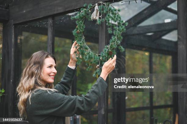 woman hangs a christmas wreath - homeowners decorate their houses for christmas stock pictures, royalty-free photos & images