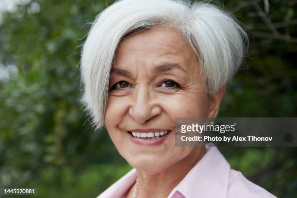 close-up portrait attractive grey-haired happy older woman standing in the summer park, front view face - beautiful armenian women fotografías e imágenes de stock