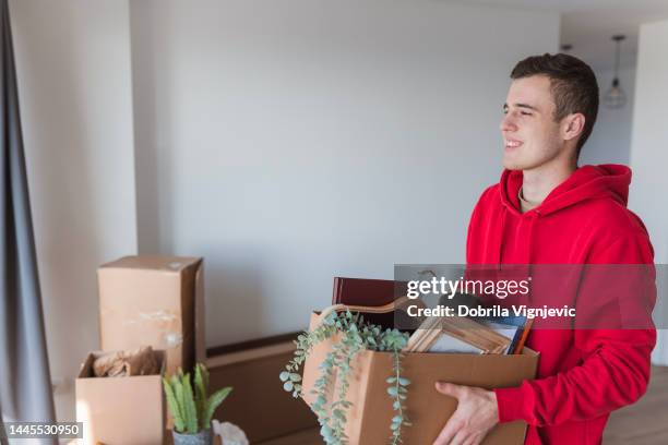 student smiling when looking through the college dorm window with a box in his hands - person on the move stock pictures, royalty-free photos & images