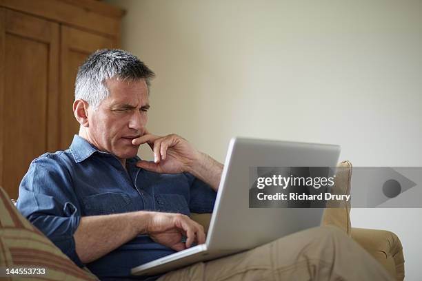 man using laptop on sofa - confusion stock-fotos und bilder