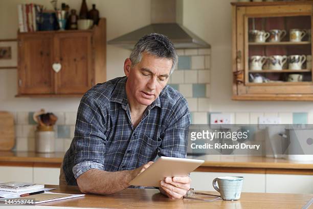 man using digital tablet in kitchen - chemise à carreaux photos et images de collection