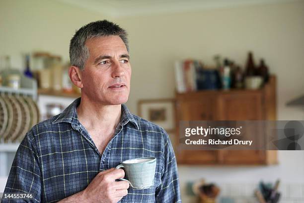 man holding coffee cup in kitchen - mature men stock pictures, royalty-free photos & images
