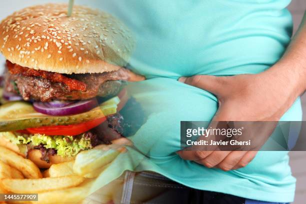 obesity and junk food. man holding his belly fat and full burger. - fettgewebezelle stock-fotos und bilder