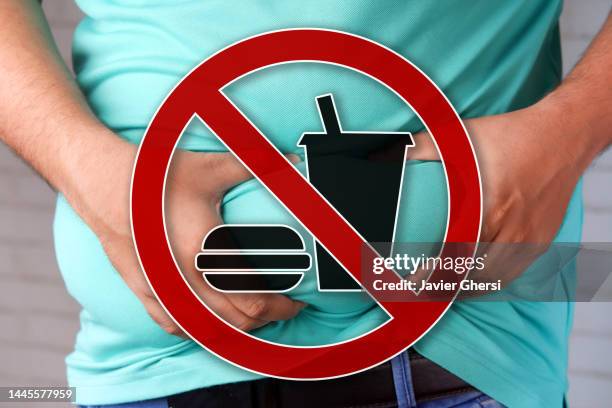 obesity and junk food. man clutching his abdomen fat and forbidden symbol. - transfettsäure stock-fotos und bilder