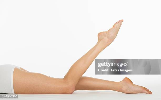 studio shot of young woman's legs - woman lying on stomach with feet up fotografías e imágenes de stock