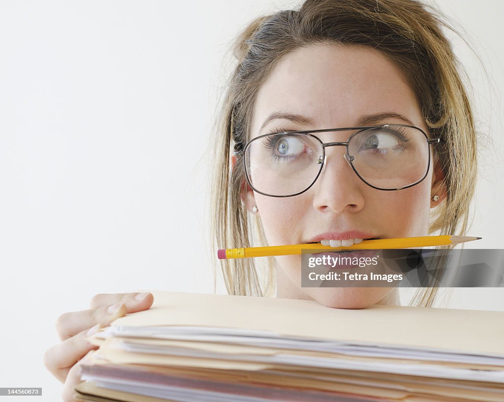 Portrait of young woman wearing glasses and holding pencil in mouth,  studio shot