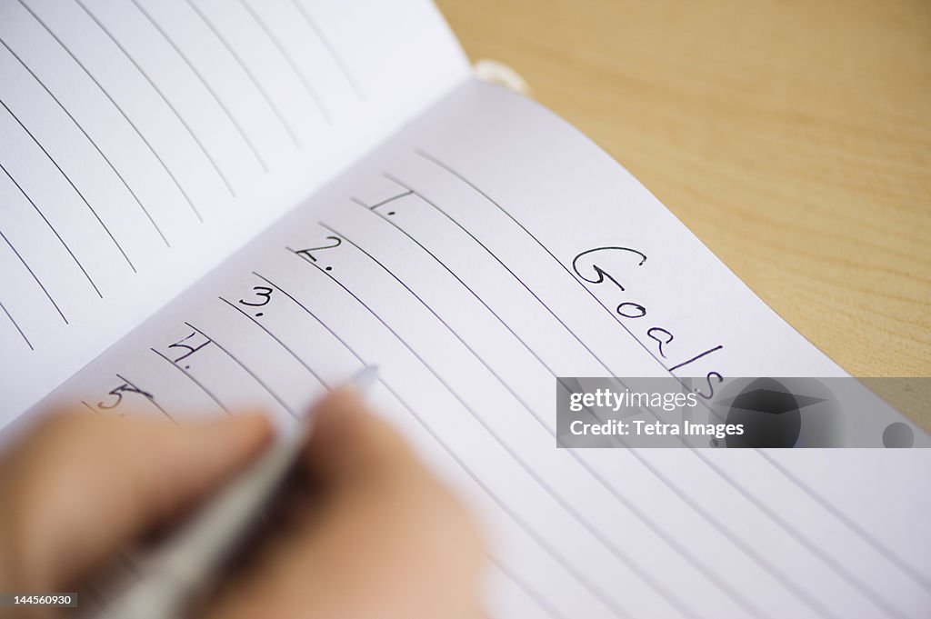 Close up of  man's hand writing New Years resolution in notebook, studio shot