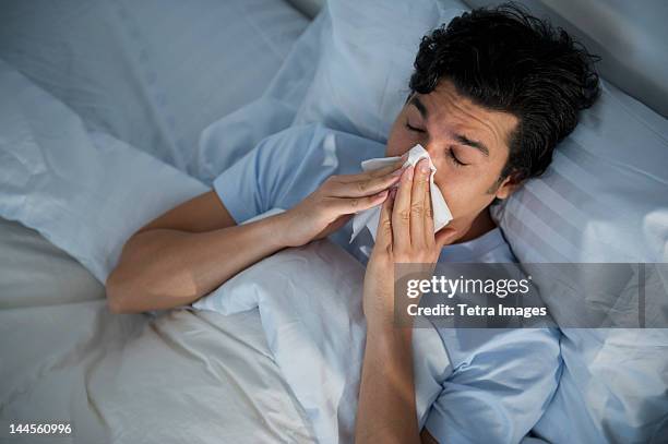 USA, New Jersey, Jersey City, man lying in bed and blowing nose