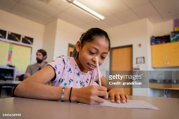 happy elementary age girl in school writing a paper with a pencil in the classroom in monument valley utah - indian society and daily life stockfoto's en -beelden