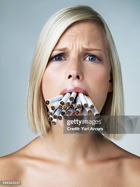 studio portrait of young woman with mouthful of cigarettes - stuffing photos et images de collection