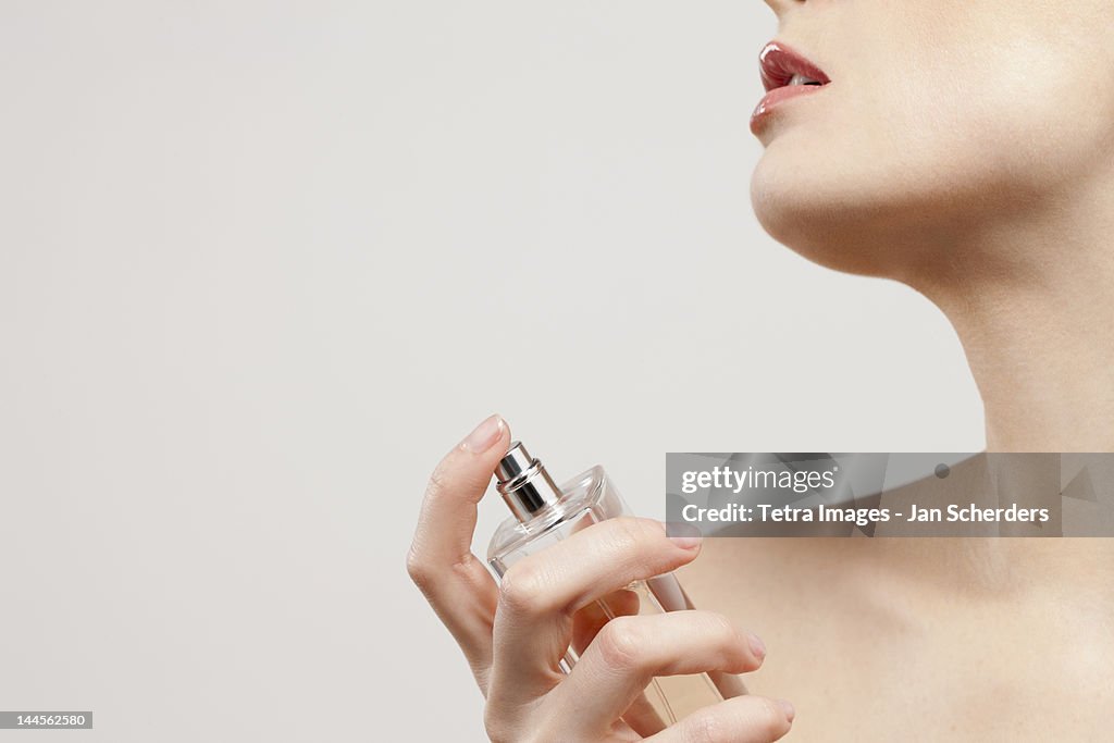 Close up of beautiful young woman spraying perfumes, studio shot