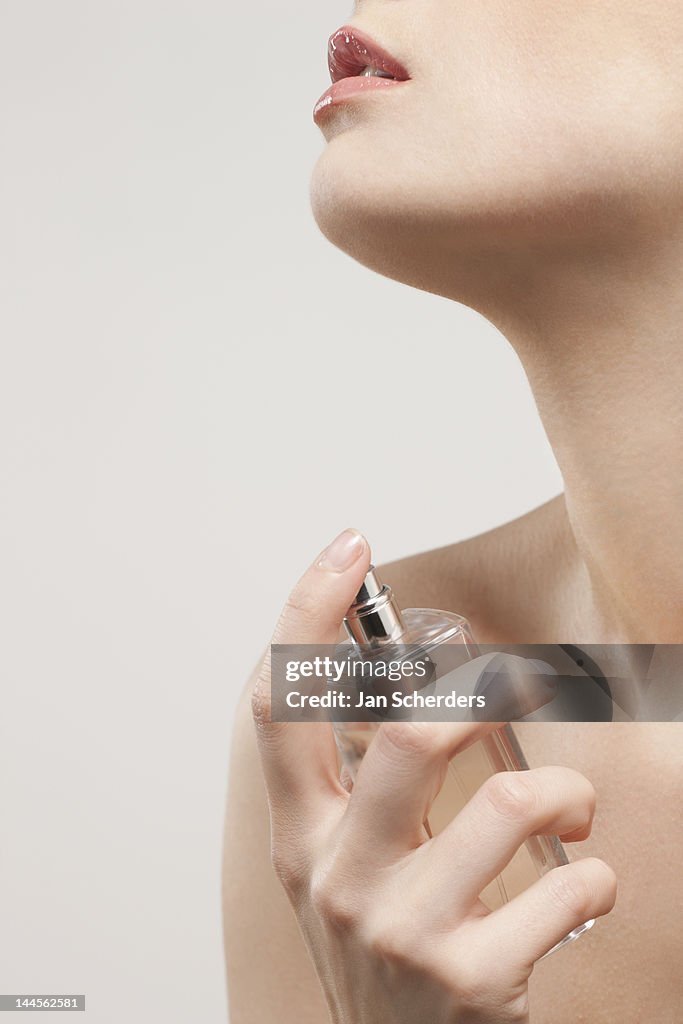 Close up of beautiful young woman spraying perfumes,  studio shot