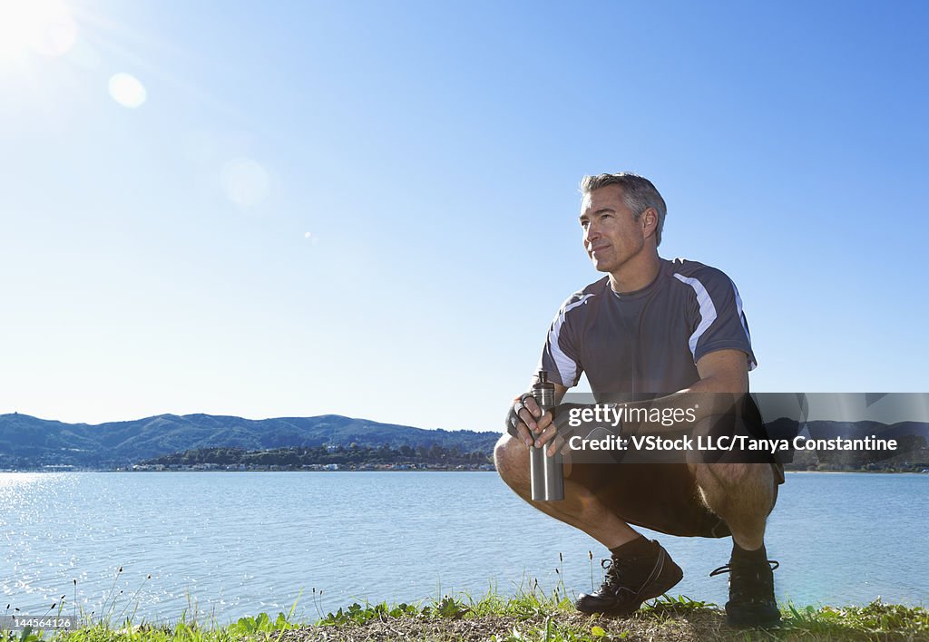USA, California, Tiburon, Man in sports clothing crouching at lakeshore with bottle of water
