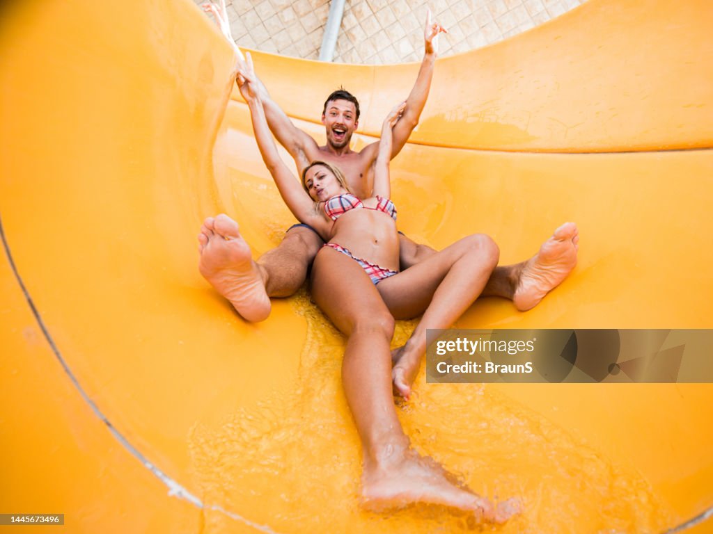 Young cheerful couple having fun on a water slide at amusement park.
