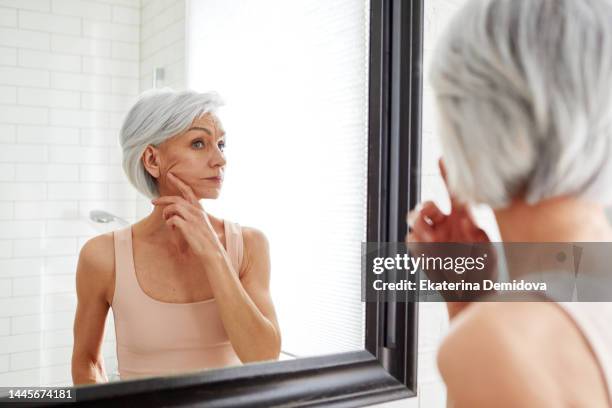 elderly woman at mirror in bathroom - antiarrugas fotografías e imágenes de stock