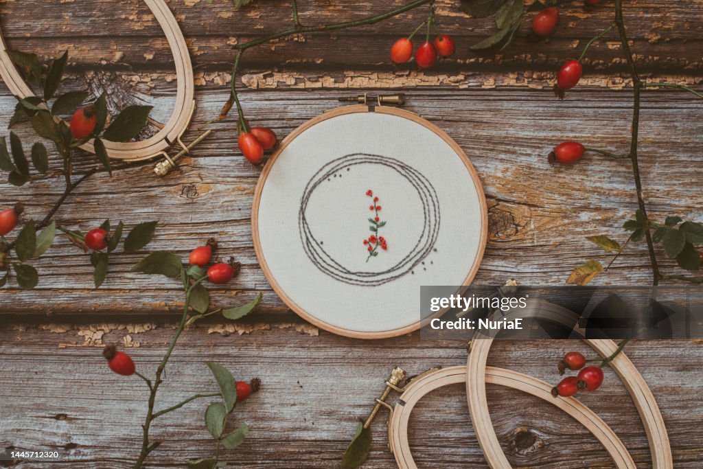 Overhead view of embroidery hoop on wooden table with rosehips