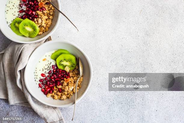 overhead view of two bowls of yogurt with granola, kiwi fruit and pomegranate - foodstyling stock-fotos und bilder