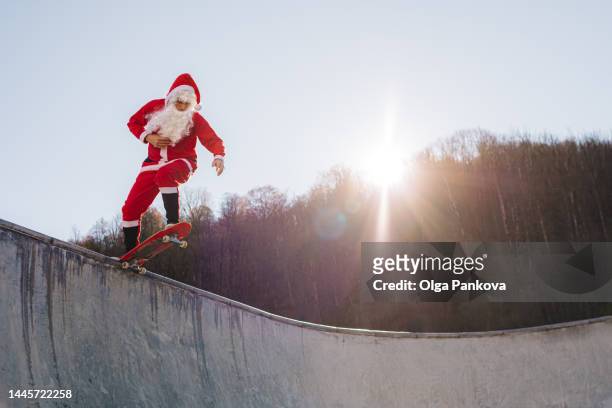male skater dressed in a santa claus costume rides in a skatepark on a sunny day - santa riding stock pictures, royalty-free photos & images