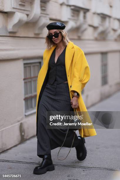 Karin Teigl is seen wearing Marc Cain barett black leather hat, Zara black two piece, black sunglasses, Prada yellow coat, Chanel black bag, Bottega...