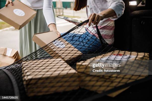 two young women loading packages in the car trunk, using a mesh liner to hold it in place - vrachtruimte stockfoto's en -beelden