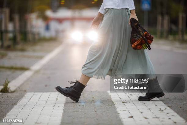mujer joven con una falda fluida llevando una bolsa de malla con comestibles y cruzando la calle - falda blanca fotografías e imágenes de stock