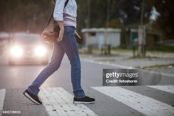 side view of unrecognizable young woman walking across the crosswalk with car headlights in the background - i was turning into a vegetable stock pictures, royalty-free photos & images