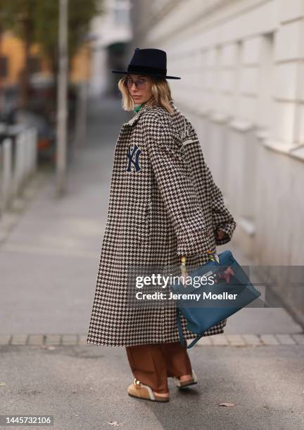 Karin Teigl is seen wearing Nomads Modern black hat, Gucci NY Yankees beige checked coat, Gestuz brown leather pants, JW Anderson beige fluffy gold...