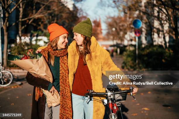 two women on bikes on a sunny street - blumenstrauß stock-fotos und bilder