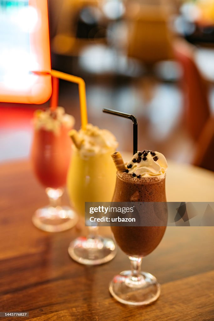 Strawberry, Vanilla And Chocolate Milkshake On A Table In A Café