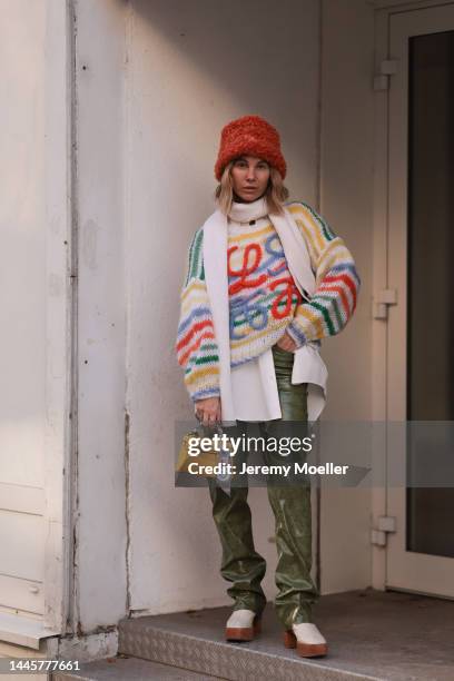 Karin Teigl is seen wearing Cult Gaia orange fluffy hat, Alpha Tauri white wool scarf, Loewe white and colorful knit sweater, Balenciaga white button...