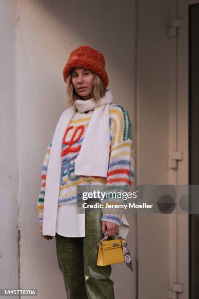 Karin Teigl is seen wearing Cult Gaia orange fluffy hat, Alpha Tauri white wool scarf, Loewe white and colorful knit sweater, Balenciaga white button...