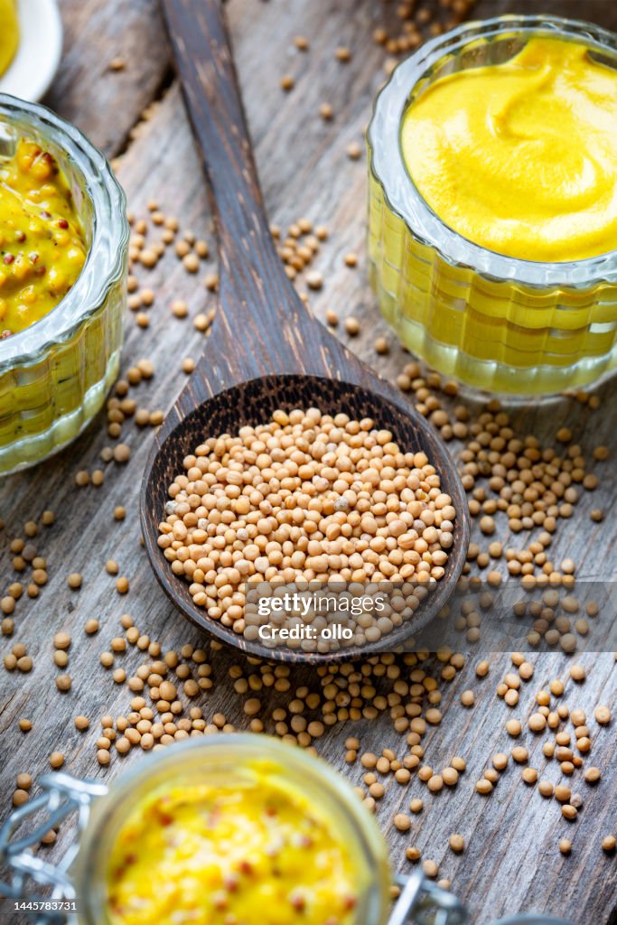 Different types of mustard and mustard seeds on a rustic wooden board