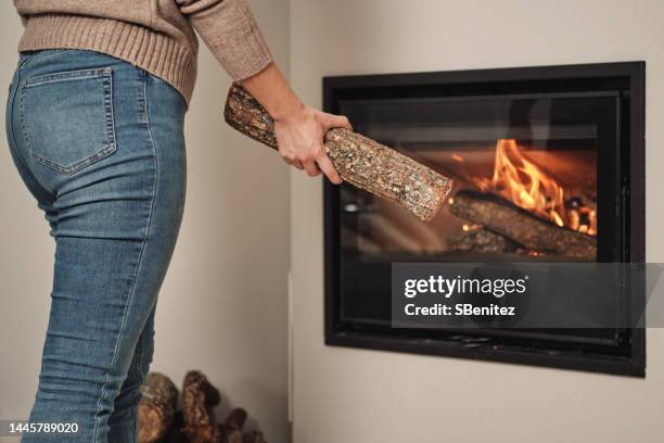 woman putting wood in fireplace - fireplace wood basket stock pictures, royalty-free photos & images