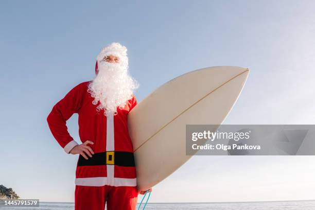 surfer dressed in santa claus costume with surfboard on the beach - surfing santa stock pictures, royalty-free photos & images