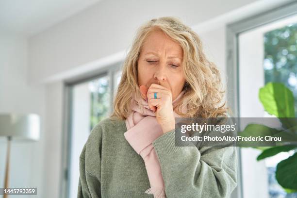 senior woman sitting indoors while coughing - virus grippal photos et images de collection