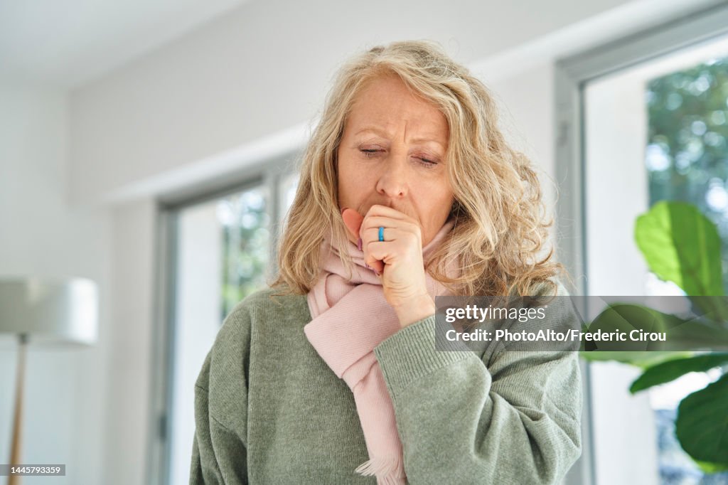 Senior woman sitting indoors while coughing